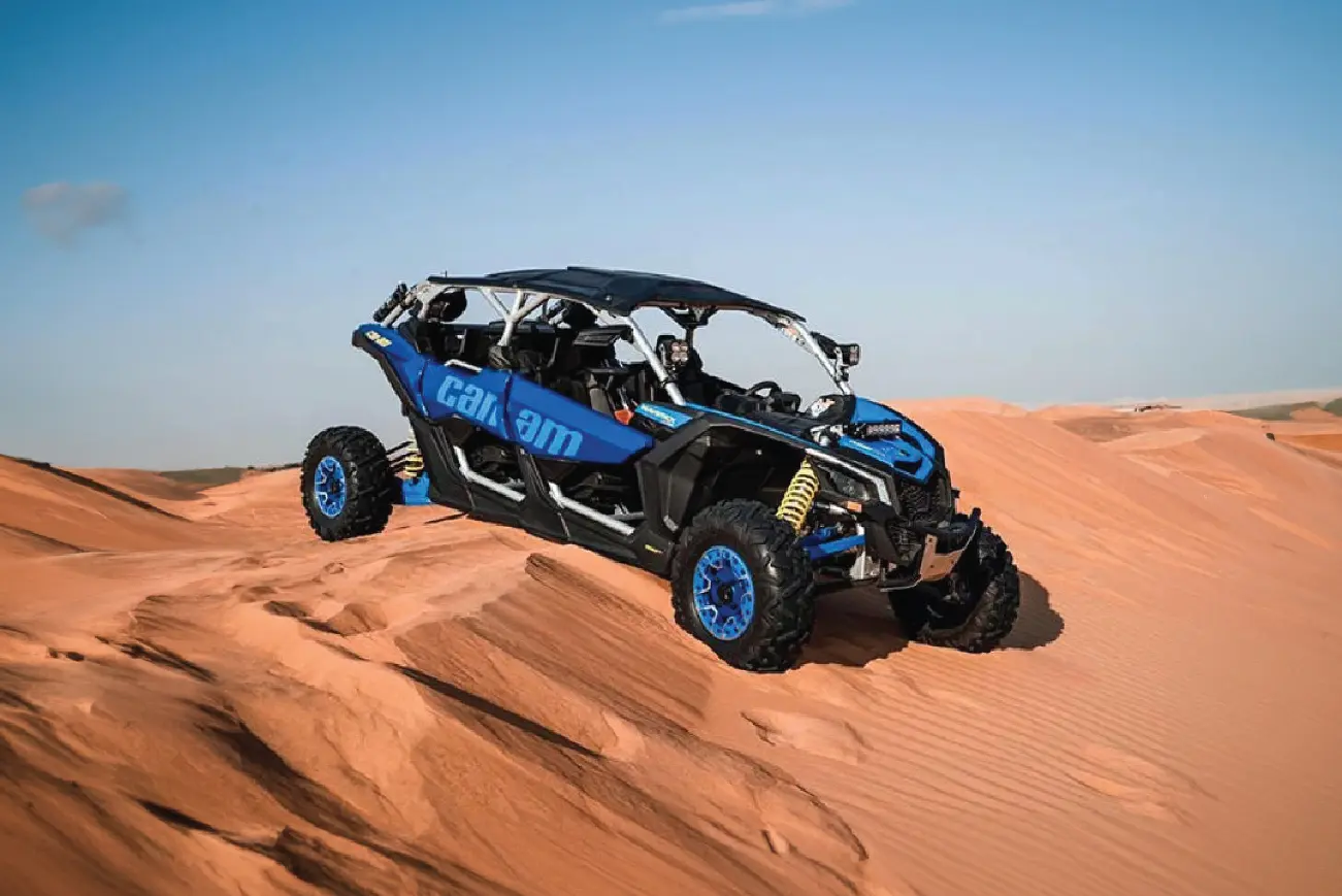 Blue Can-Am buggy crossing a dune ridge